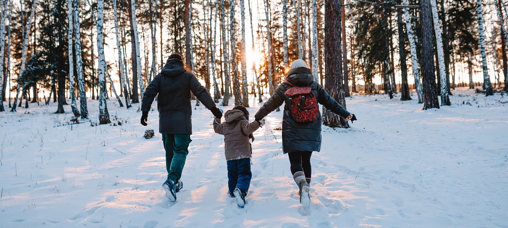 2 adults and a child running in the snow towards some trees